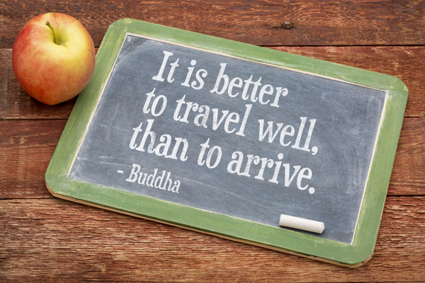 It is better to travel well than arrive - Buddha quote on a slate blackboard against red barn wood