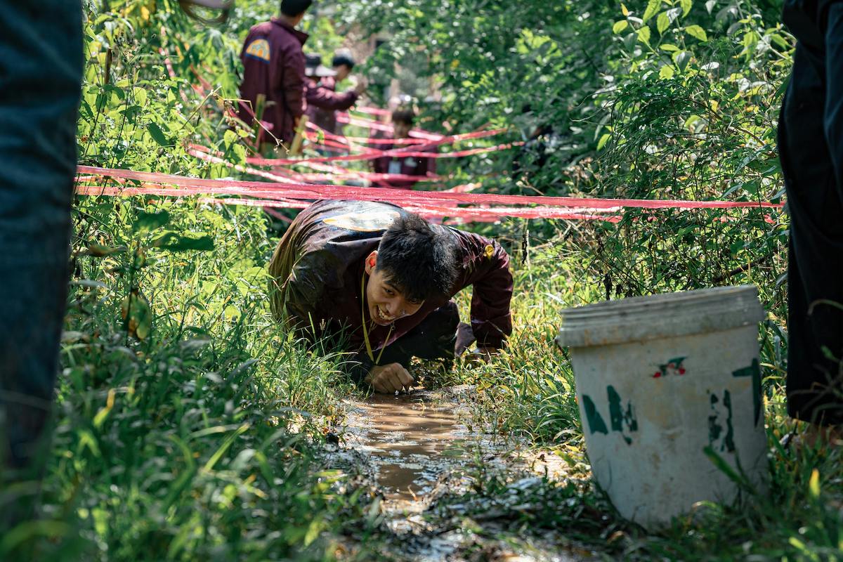 A teenager crawling under rope in the forest smiling