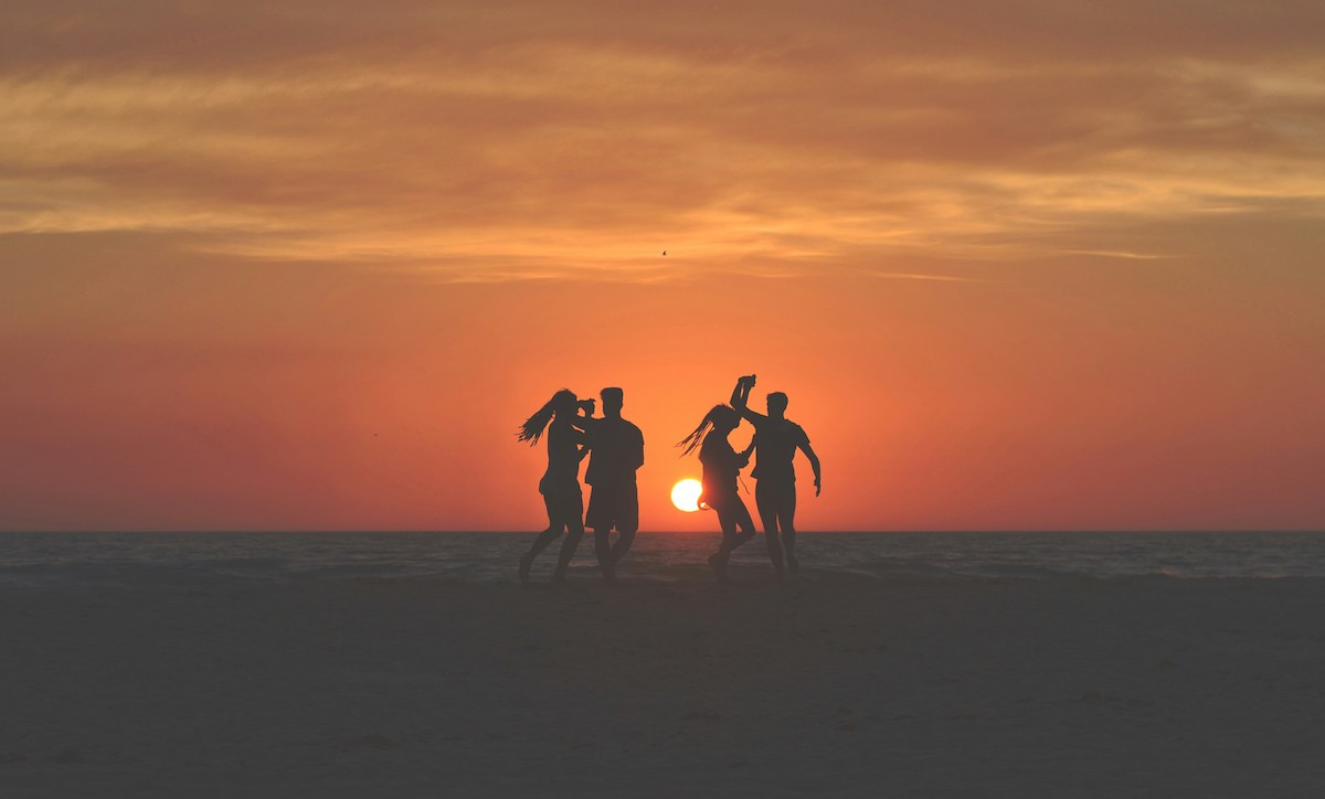 silhouette-photo-of-four-people-dancing-on-sands-near-shoreline