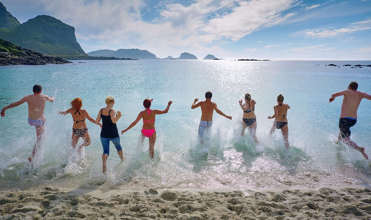 Group of people running into the ocean on a sandy beach