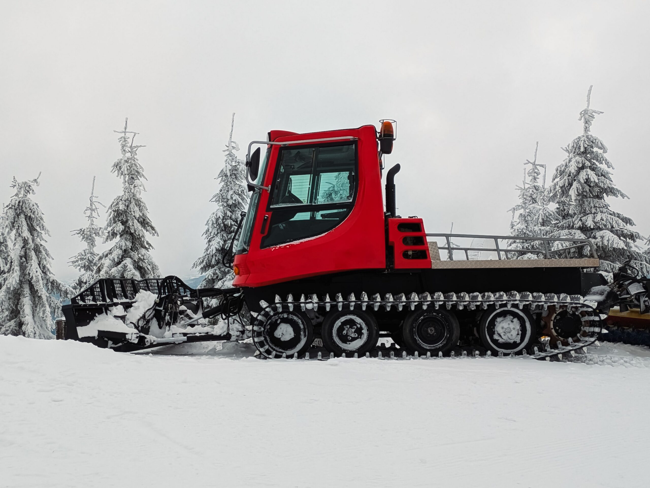 A red snowcat vehicle prepares ski slopes on a snowy mountain landscape.